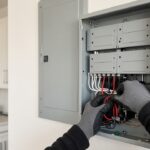Electrician wiring a backup power subpanel beside the main panel