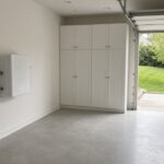 Wall-mounted home battery beside the main panel in a tidy two-car garage
